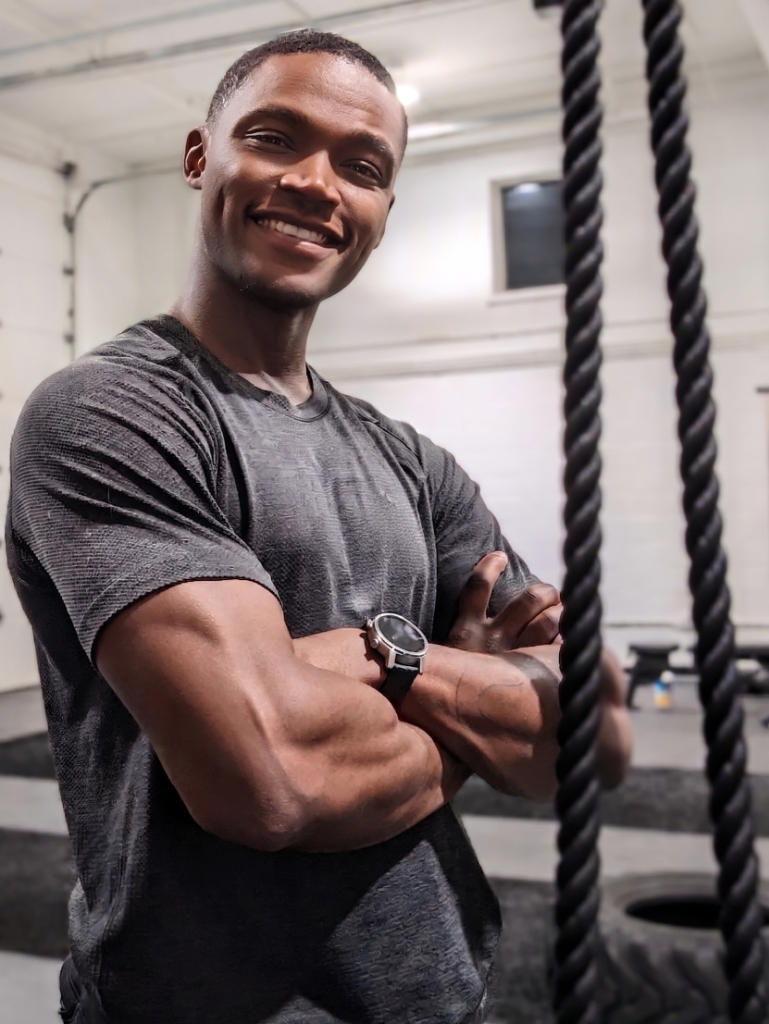 Personal Trainer Grayson smiling in an active home gym setting with training ropes